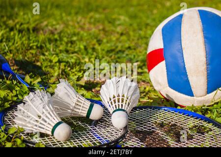 Three shuttlecocks, badminton rackets and a volleyball ball on the grass close-up. Selective focus. Space for the text. The concept of outdoor sports Stock Photo