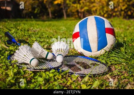 Badminton rackets, shuttlecocks and a volleyball ball lie in the park on the grass. The concept of outdoor sports games Stock Photo