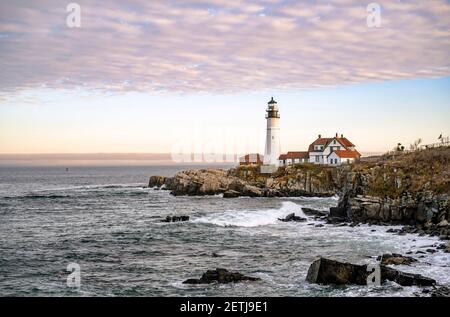 Lighthouse illuminated by the setting sun on a rocky promontory against the backdrop of a cloudy sky on the Atlantic coast in Portland Maine New Engla Stock Photo