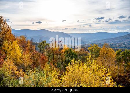 A mesmerizing colorful atmospheric landscape with an autumn maple grove in yellow and red tones and a panorama of a valley with a provincial town at t Stock Photo