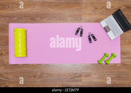 Fitness mat, dumbbells, expander and laptop for online workouts at home. Online learning concept in relation to the pandemic Stock Photo