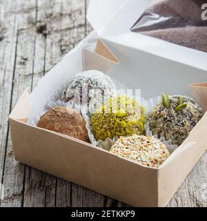 Healthy energy balls made of dried fruits and nuts with coconut chips, cacao, flax seeds, pistachios, sesame. Raw vegan candy in paper box on wooden t Stock Photo
