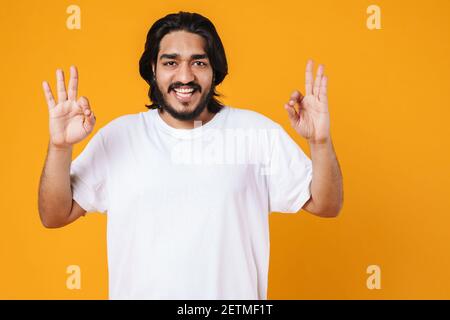 Happy young casual indian man standing isolated over yellow background, showing ok gesture Stock Photo