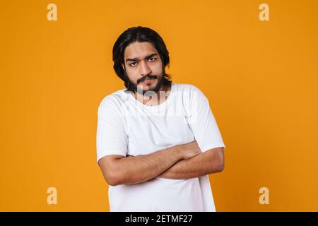 Upset indian man standing with folded hands isolated over yellow background Stock Photo