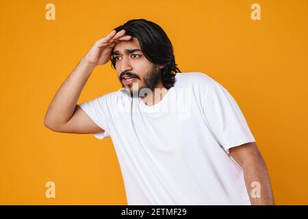 Upset young indian man looking far away with hand over head. Searching concept Stock Photo