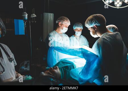 An international professional team of surgeon, assistants and anesthesiologist perform a complex operation on a patient under general anesthesia. Dark Stock Photo