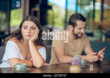 Sad turning away woman and cheerful man with smartphone Stock Photo
