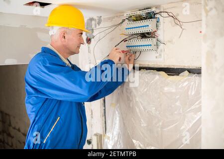 Senior electrotechnician connecting wiring system and completing the preparation of the electrical circuit home network Stock Photo