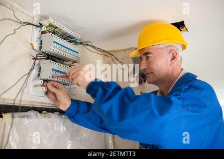 Senior electrotechnician connecting wiring system and completing the preparation of the electrical circuit home network Stock Photo