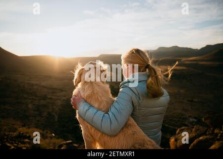 Caucasian young teen hugging golden puppy while gazing into horizon during vibrant sunset  Stock Photo