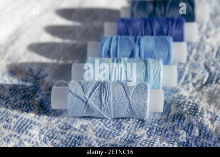 Set of sewing thread coils on white natural fabric with embroidery. Blue thread. Several reels of thread in different shades of blue. Background Stock Photo