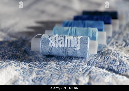 Blue thread. Set of sewing thread coils on white natural fabric with embroidery. Several reels of thread in different shades of blue. Selective focus. Stock Photo