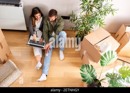 Moving in break with a laptop, young couple resting on the floor Stock Photo