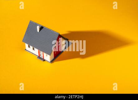 A small model house on a warm yellow ground casts a long shadow Stock Photo