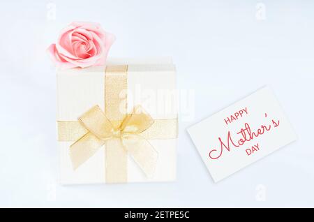 White box with gift inside wrapped in gold ribbon with abow, on the box lies pink rose in front of white background. Holiday gift valentine day, 14 Stock Photo