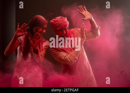 A HAPPY YOUNG WOMAN AND MAN RAISING HANDS TO SHIELD THEMSELVES FROM COLOURS BEING THROWN AT Stock Photo