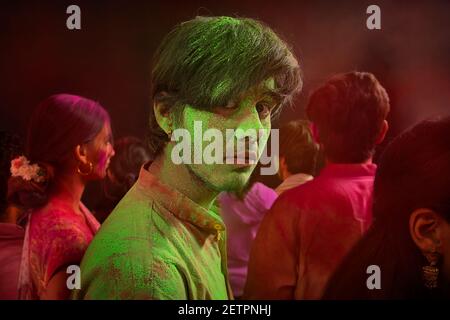 A YOUNG MAN WITH GULAL ALL OVER HIS FACE TURNING AROUND AND SERIOUSLY LOOKING WHILE STANDING IN A CROWD Stock Photo