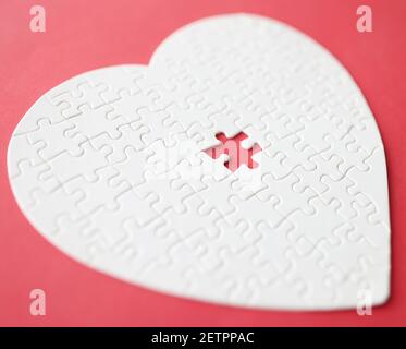 White heart made from puzzle lying on red background Stock Photo