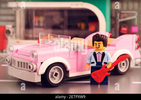 Tambov, Russian Federation - January 22, 2020 Lego rock-n-roll star minifigure with guitar near his pink 1950s-style convertible in Lego street. Stock Photo