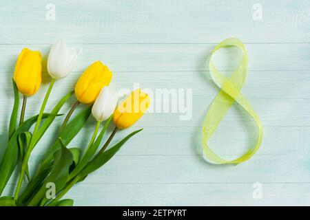 March 8, Women's Day, Mother's Day greeting card with yellow and white tulips on a wooden background. Top view, flat layout. Figure 8 with a silk ribb Stock Photo