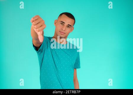 Cool young latin man with thumb down over green background. Stock Photo