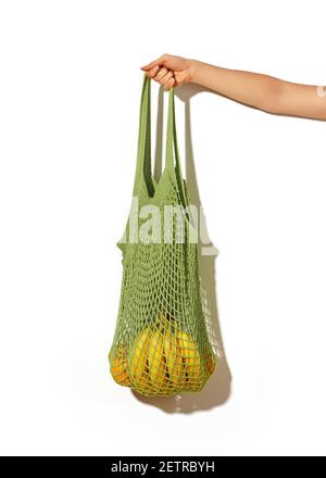 Woman hand holding green lime string shopping bag with vegetables and fruits in front of white wall background. Eco lifestyle. No more plastic Stock Photo