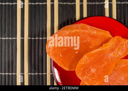 Large slices of dried mango in a red saucer on a bamboo mat, close up. Stock Photo