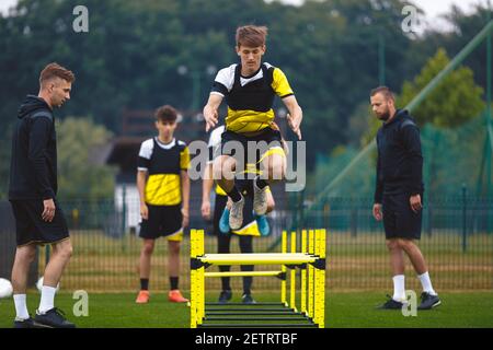 Youth Soccer Team on Training. Young Boys in Football Club Practicing Durability. Teenage Boy Jumping High Over Hurdle Obstacles. Young Men Coaching S Stock Photo