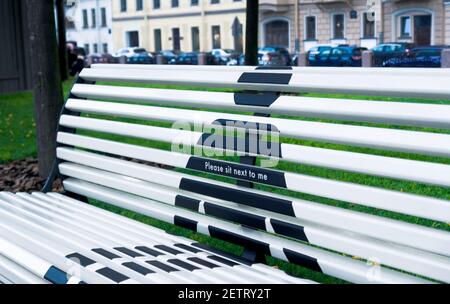 Concept of social distance of bench in public park, showing a shape of person with inscription please sit next to me Stock Photo