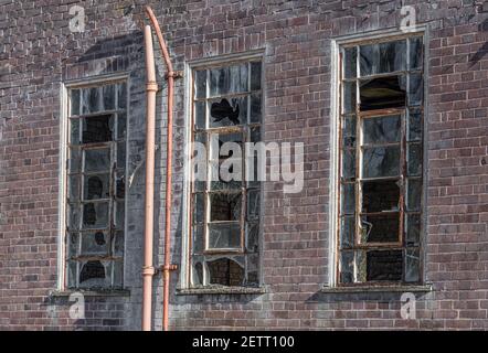 A close up of three broken old windows on a derelict abandoned building. All of the glass panes have been broken Stock Photo