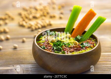 Homemade chickpea green hummus with herbs in round bamboo bowl, celery, carrot sticks on wood Stock Photo