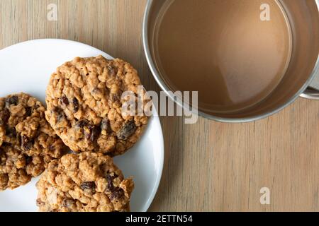 Overhead view of two homemade oatmeal raisin cookies on a white plate with coffee atop a table. Stock Photo