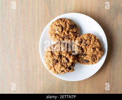 Overhead view of two homemade oatmeal raisin cookies on a white plate atop a table. Stock Photo