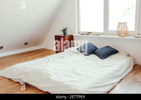 Minimalist white bed mattress on solid hardwood oak floor in cozy modern home bedroom. Minimalist white bright room. Stock Photo
