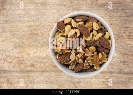 Assorted nuts in a white bowl atop an old wood cutting board top view. Stock Photo