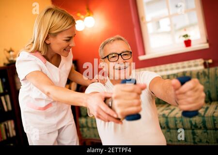 Senior mature man doing exercises with dumbbells while nurse helps to them Stock Photo
