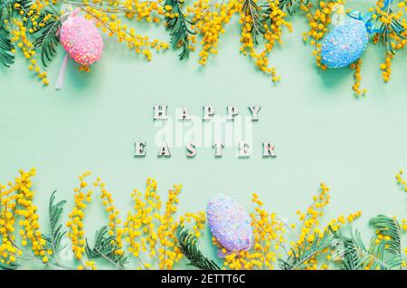 Easter background, Easter 2021 card. Easter eggs, mimosa flowers, Happy Easter inscription on the green background Stock Photo