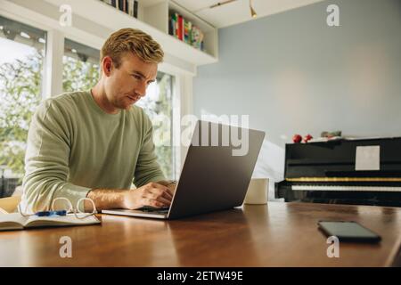 Young man sitting at table and working on laptop. Caucasian man working from home. Stock Photo