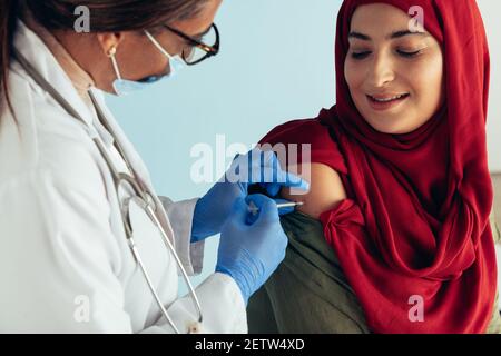 Close-up of a muslim woman getting flu shot on her arm. Female doctor giving vaccine to Islamic woman. Stock Photo