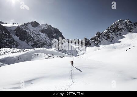 Man with backpack walking on the snow hill in the beautiful mountains against blue sky in Almaty, Kazakhstan Stock Photo