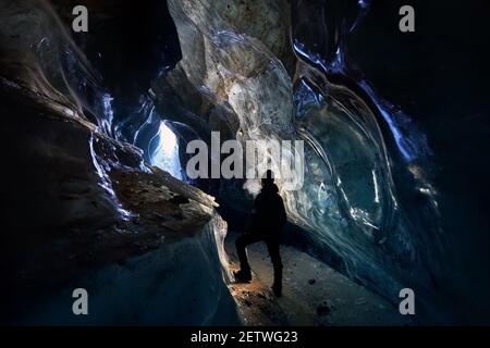 Silhouette of man exploring an amazing glacial ice cave in the mountains in Kazakhstan Stock Photo