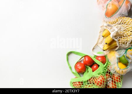 Tomatoes, lime, lemon, orange in reusable eco friendly green mesh bags on white background. Zero waste concept. Ecological shopping. Copy space. View Stock Photo