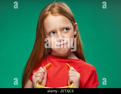 cute girl red hair gestures with hands emotions childhood school Green background Stock Photo