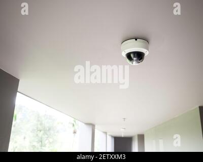 CCTV camera on white ceiling at walkway on ground floors in apartment building with copy space. Stock Photo