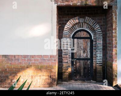 Old vintage curved wooden door ornamented with bricks on concrete building with copy space. Stock Photo