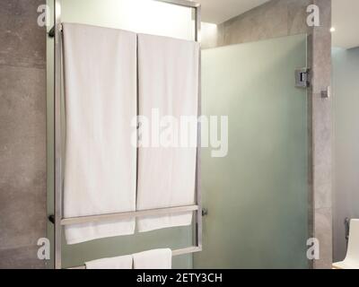 Two set of clean white towel on hanger rack in front of frosted glass shower room in modern bathroom preparing for guest in hotel. Stock Photo