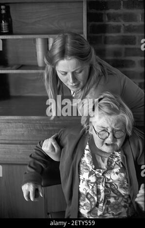 Sixteen year old school girl on work experience as a care assistant in care home. Helping elderly female resident to the chair Stock Photo