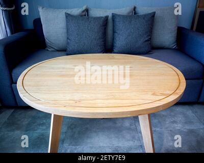 Round wooden table. Empty light brown round wood table top near blue grey sofa seat in hotel room. Stock Photo