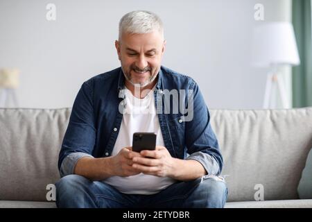 Smiling mature grey-haired man using mobile phone at home Stock Photo