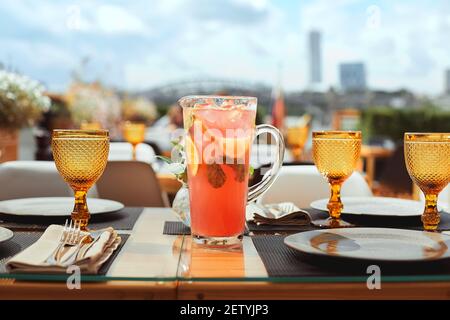 Lemonade with oranges in jug with ice bucket on white table in restaurant.